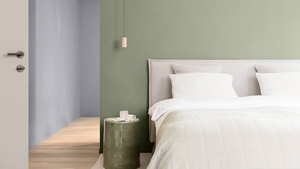 Ein Schlafzimmer mit einer grünen Akzentwand hinter dem Bett und hellgrauen Wänden auf einer Seite.