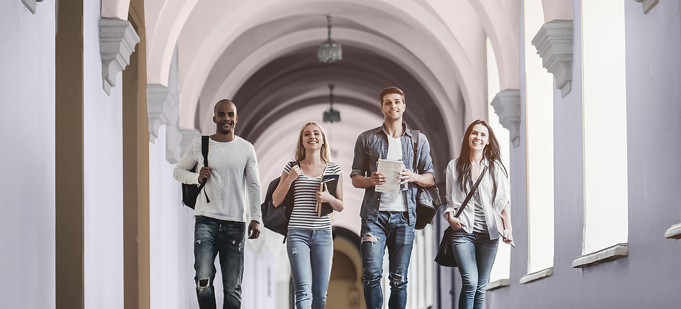 Vier Studierende gehen durch einen Gang, dessen Wände in sanftem Lila gestrichen sind.