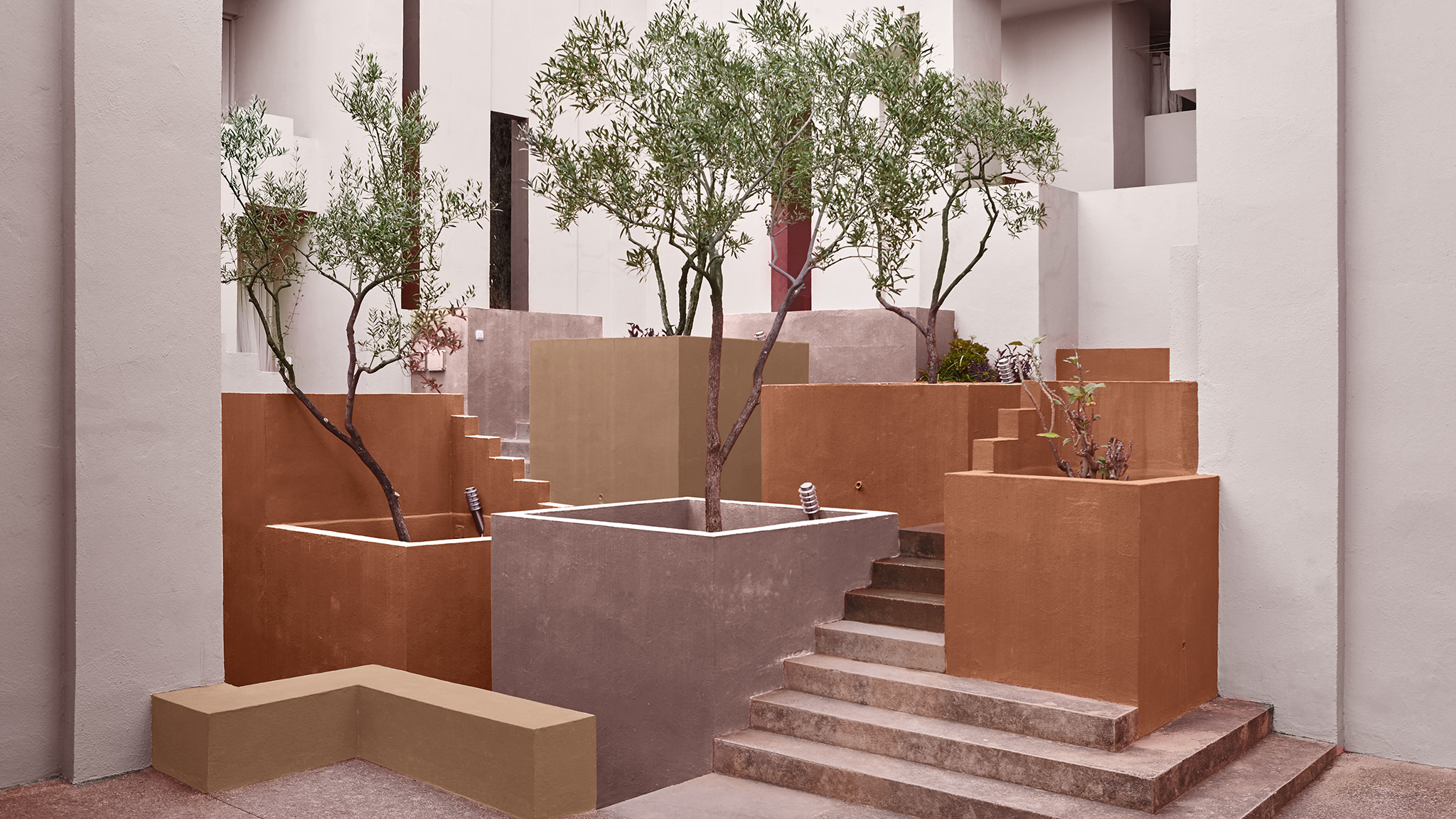 Ein Hotelaußenbereich mit Pflanzgefäßen, die in verschiedenen warmen, erdigen Farben gestrichen sind – von Rosa bis Terrakotta. 