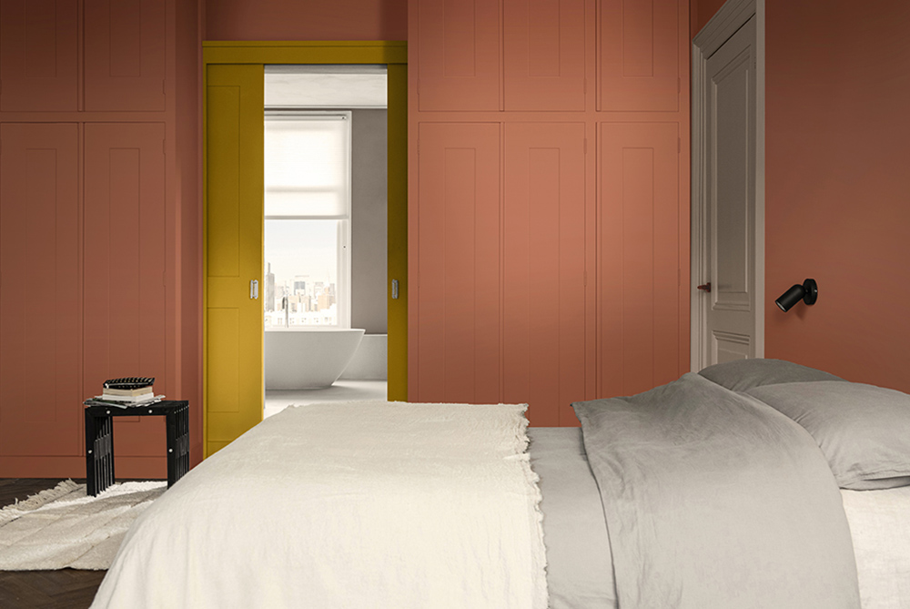 A warm and cozy hotel bedroom painted with a terracotta red and bright yellow