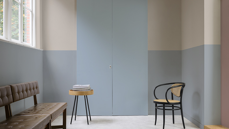 Warteraum mit grau-blauen und rosa Wänden sowie Bank, Hocker und Stuhl