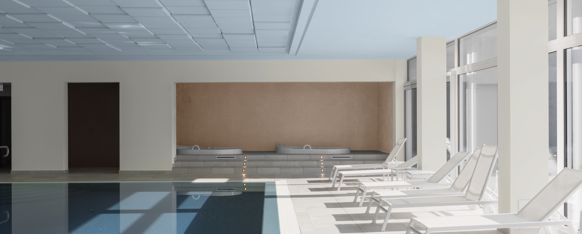 Hotelschwimmbad mit weißen Liegen und blauer Decke